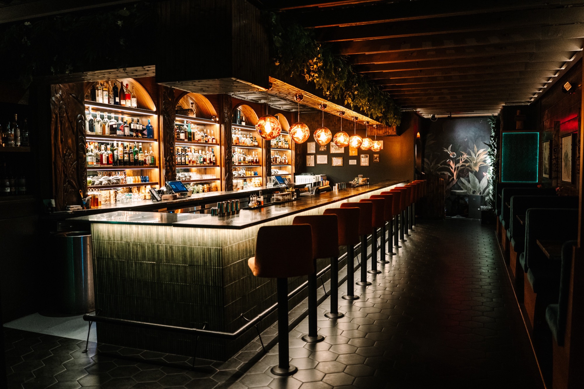 The bar at Callisto, lit shelves and copper pendants over a long row of stools