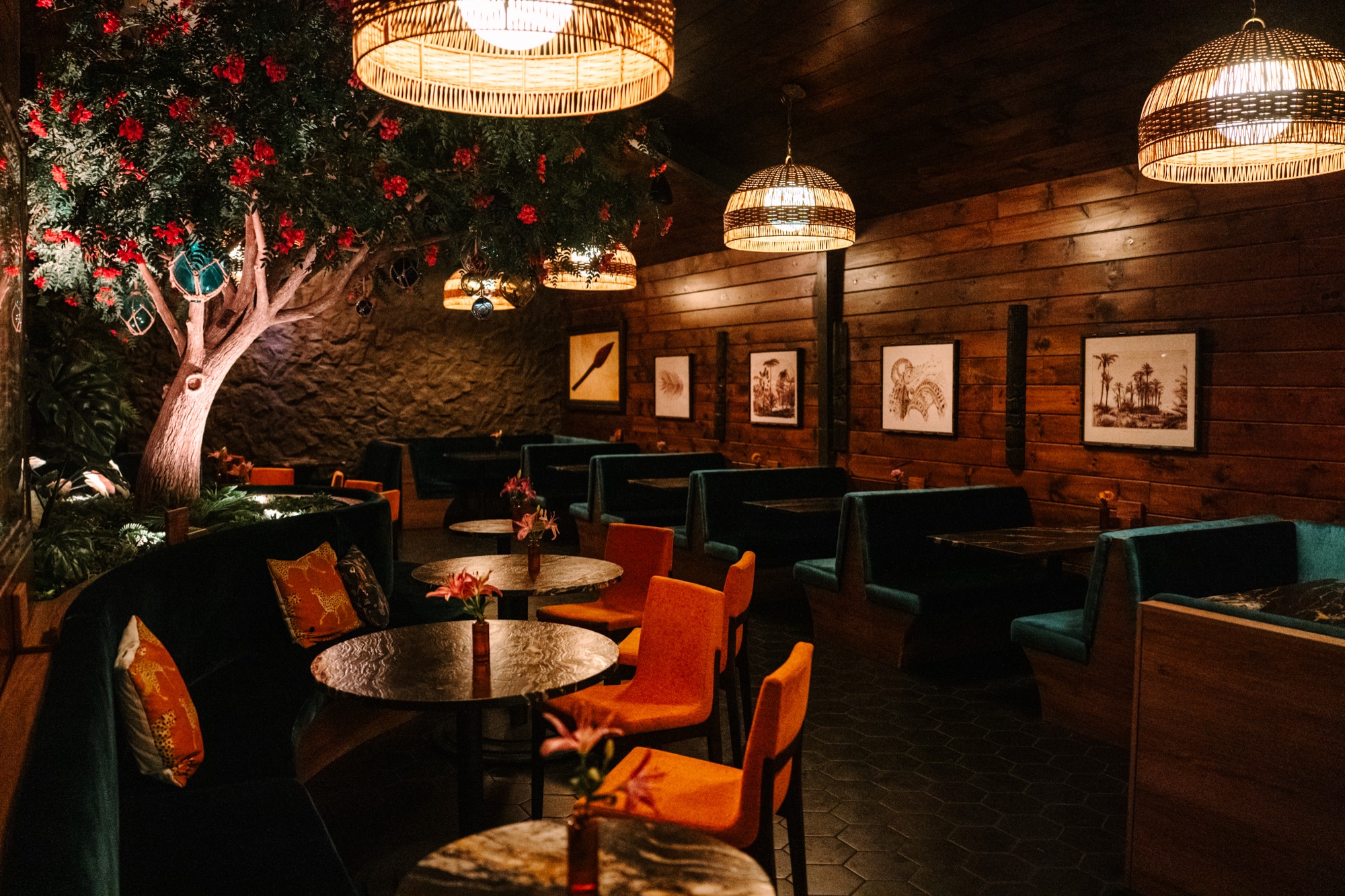 Callisto's main dining room with teal velvet booths and rattan pendants under a flowering tree